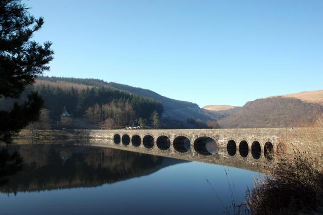 A bridge across one of the Elan Valley reservoirs reflects perfectly in the still water, along with the bright blue, crisp winter sky..
