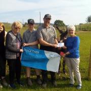 Ida Bufton, chair of the Llandrindod Wells Cancer Research UK committee, receiving the money from Stephen Powell with his family and Coco the donkey.